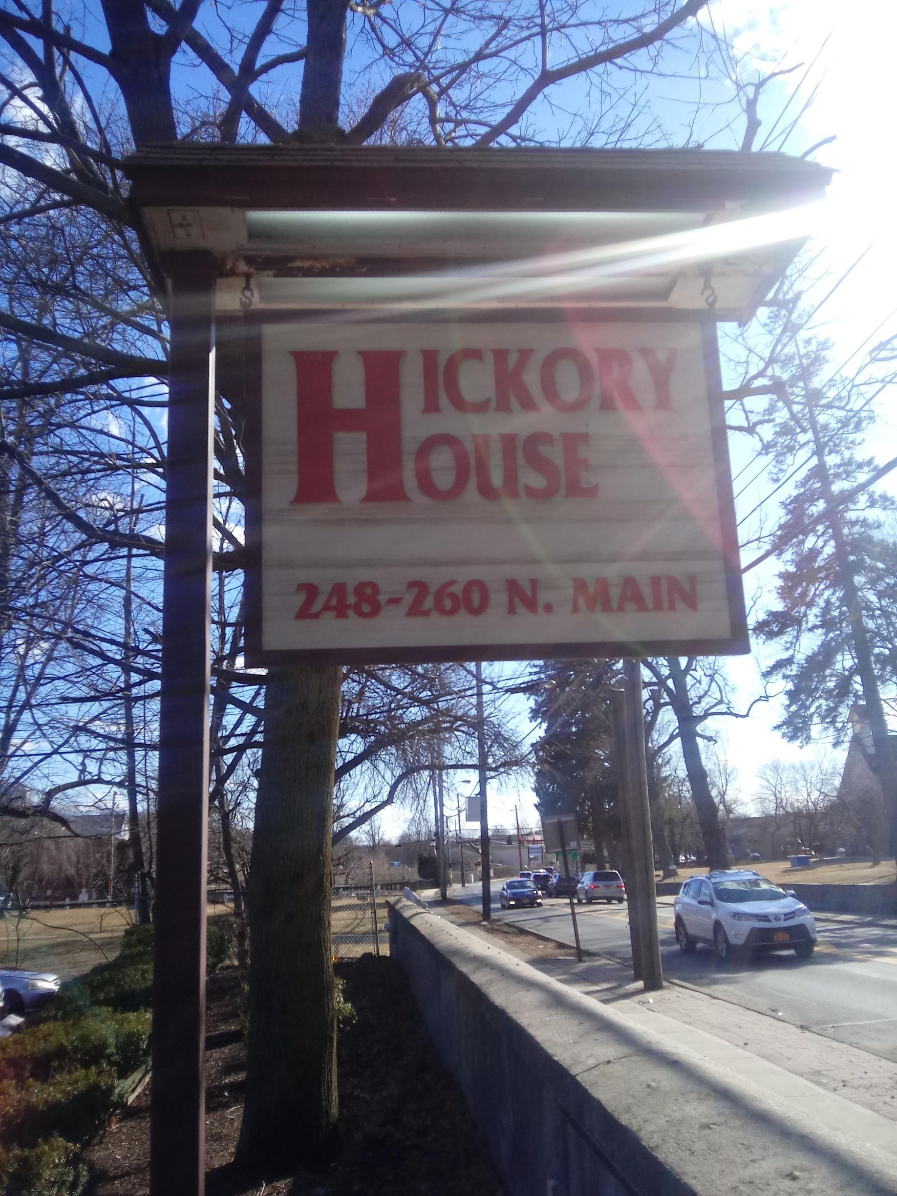 Hickory House sign on Main Street beside a sidewalk and parked cars on a sunny day