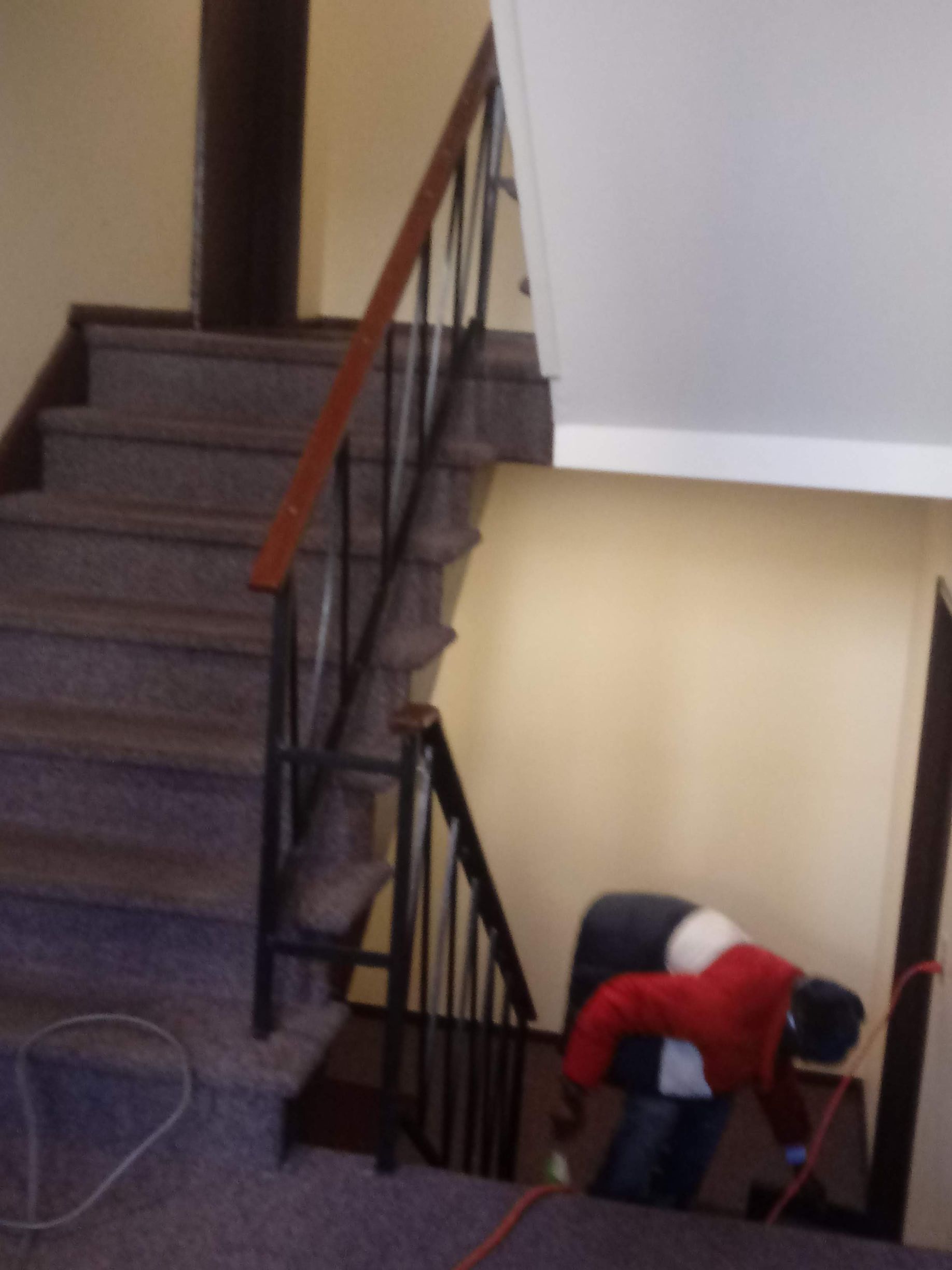 Person in red shirt bending over near a staircase indoors