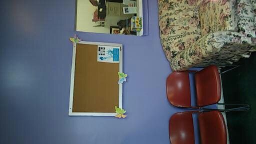 Bulletin board on a purple wall beside red chairs and a floral cushion in a room.