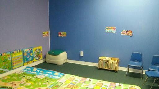 Empty playroom with blue walls, colorful floor mats, small chairs, and toy shelves.