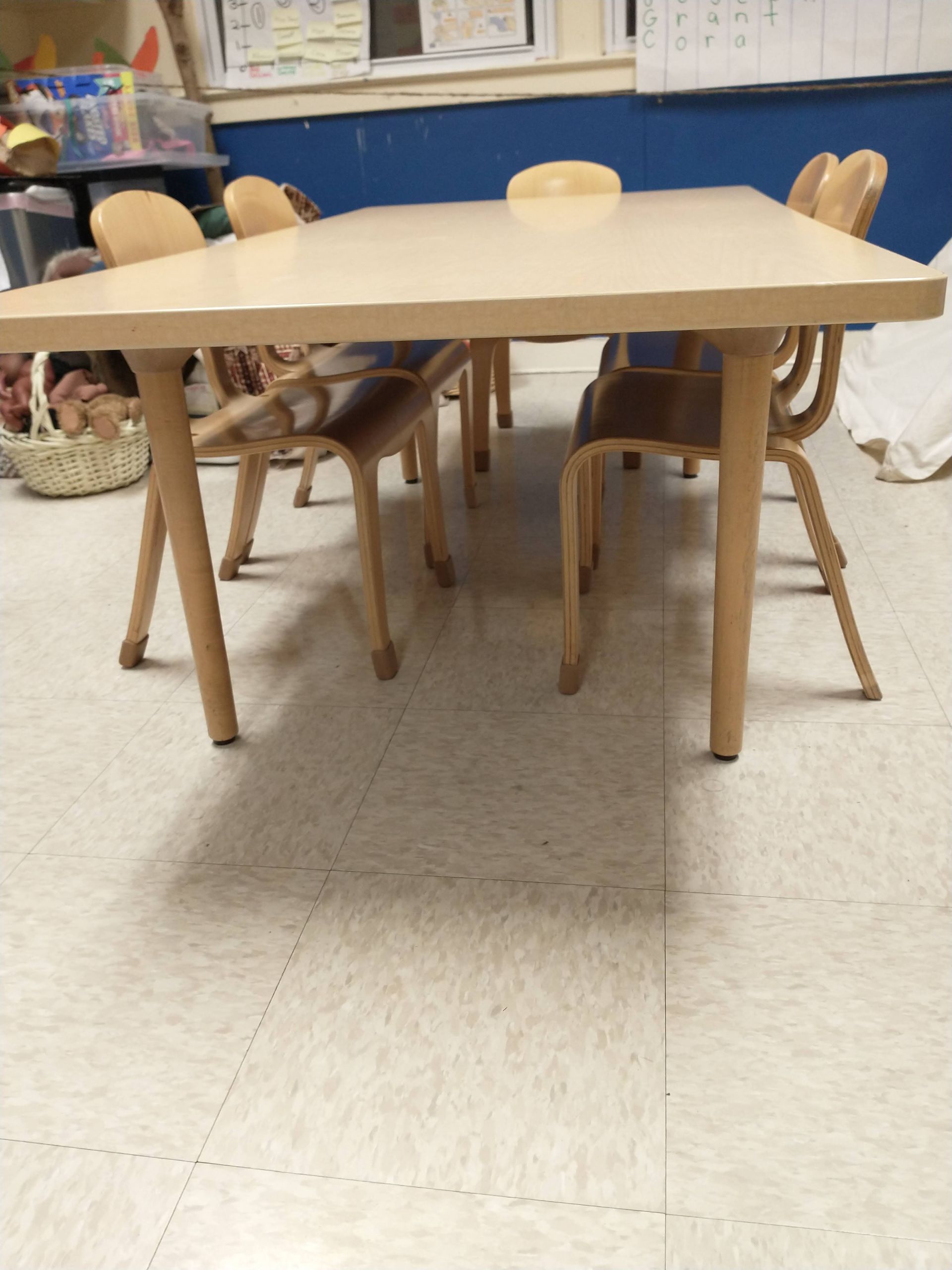 Light wood table surrounded by matching chairs in a classroom or playroom.