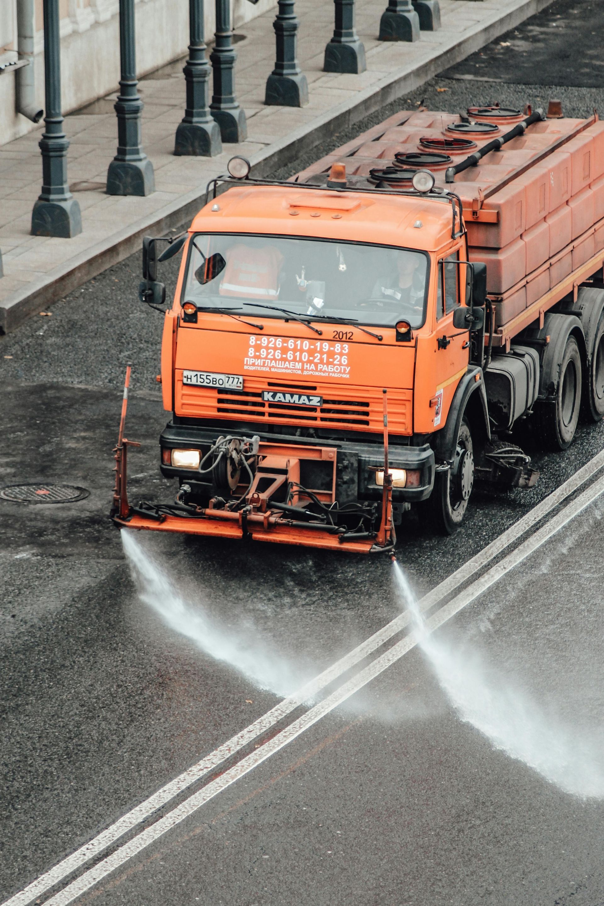 Orange street sweeper spraying water on a wet road in the rain