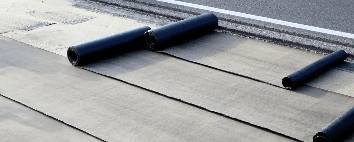 Rolls of waterproofing material are being rolled on a concrete surface.