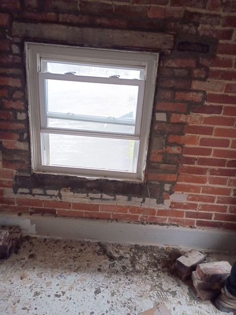 Window in a brick wall. Window frame is white. The wall is red brick. Floor is light gray concrete.