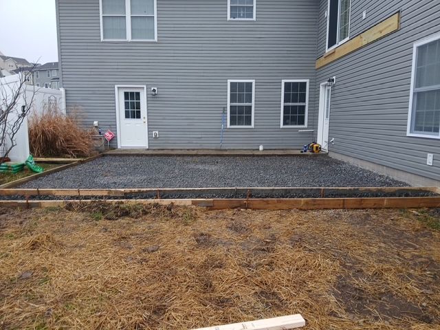 A gravel patio framed by wooden boards, set against a gray house with a white door and windows.