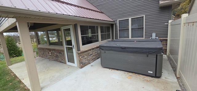 Hot tub on concrete patio next to a house with a screened-in porch.