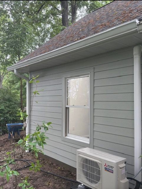 Exterior view of a light green house with a window, white gutters, and an air conditioning unit.