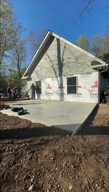 New house construction, concrete patio. Workers near the building with light green siding and windows.