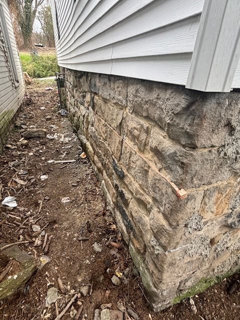 Stone foundation of a house with white siding and a narrow dirt yard. Stone foundation of a house with white siding and a narrow dirt yard.