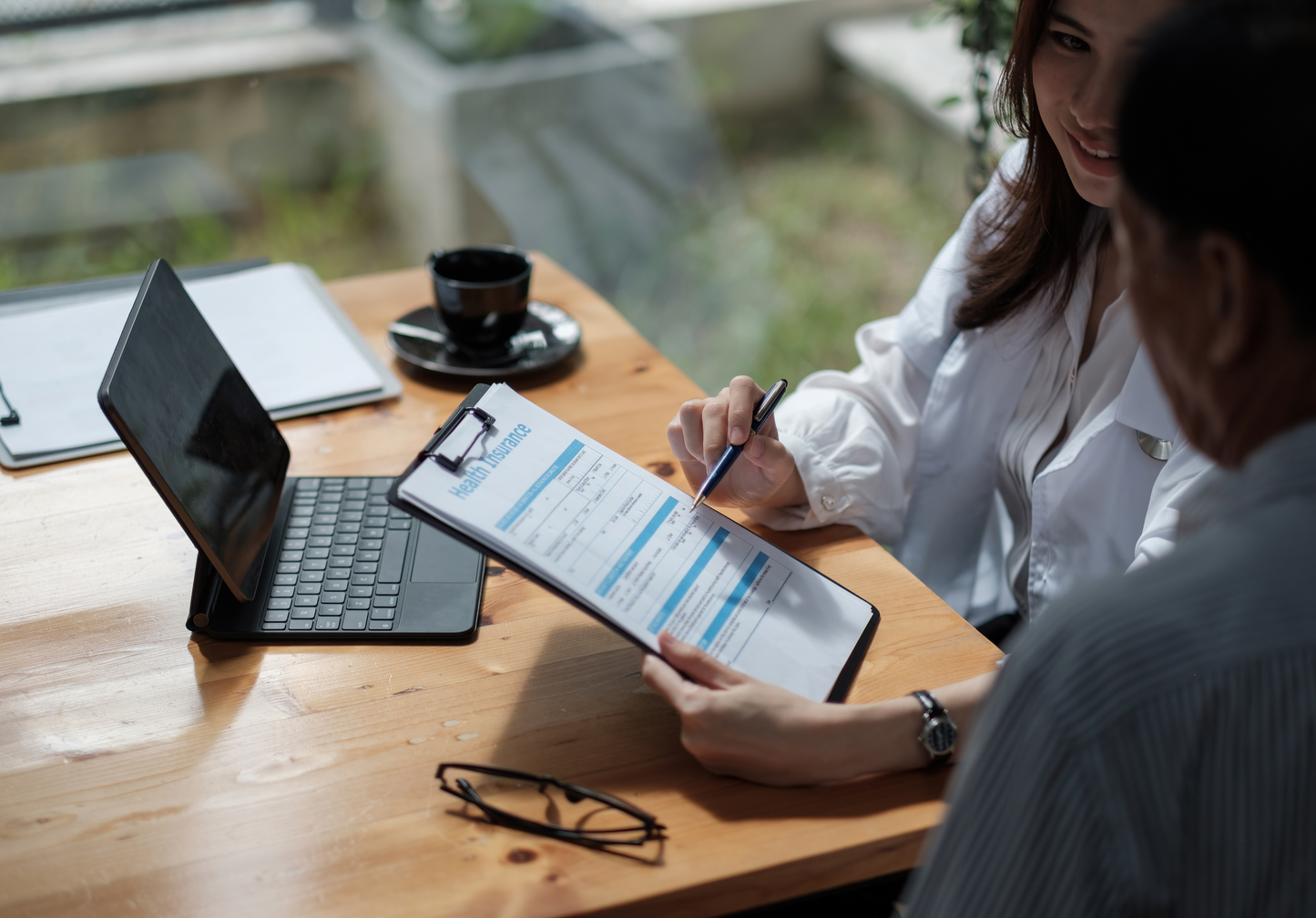 A man and a woman are sitting at a table looking at a clipboard.