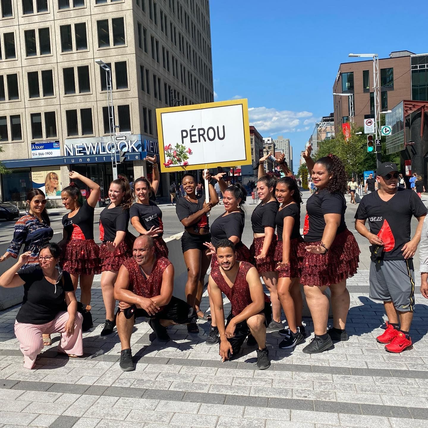 Group of people in traditional Peruvian attire posing on a city street, holding a sign that says
