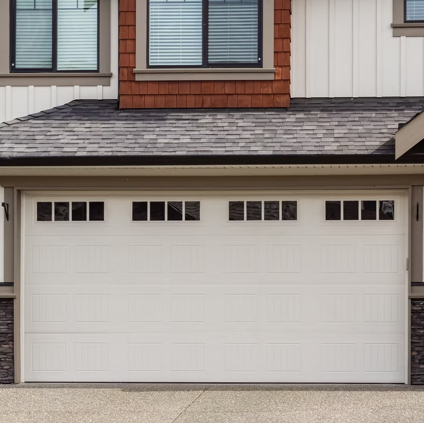 A white garage door is sitting in front of a brick house.