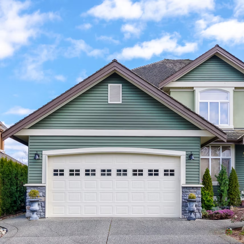 A green house with a white garage door