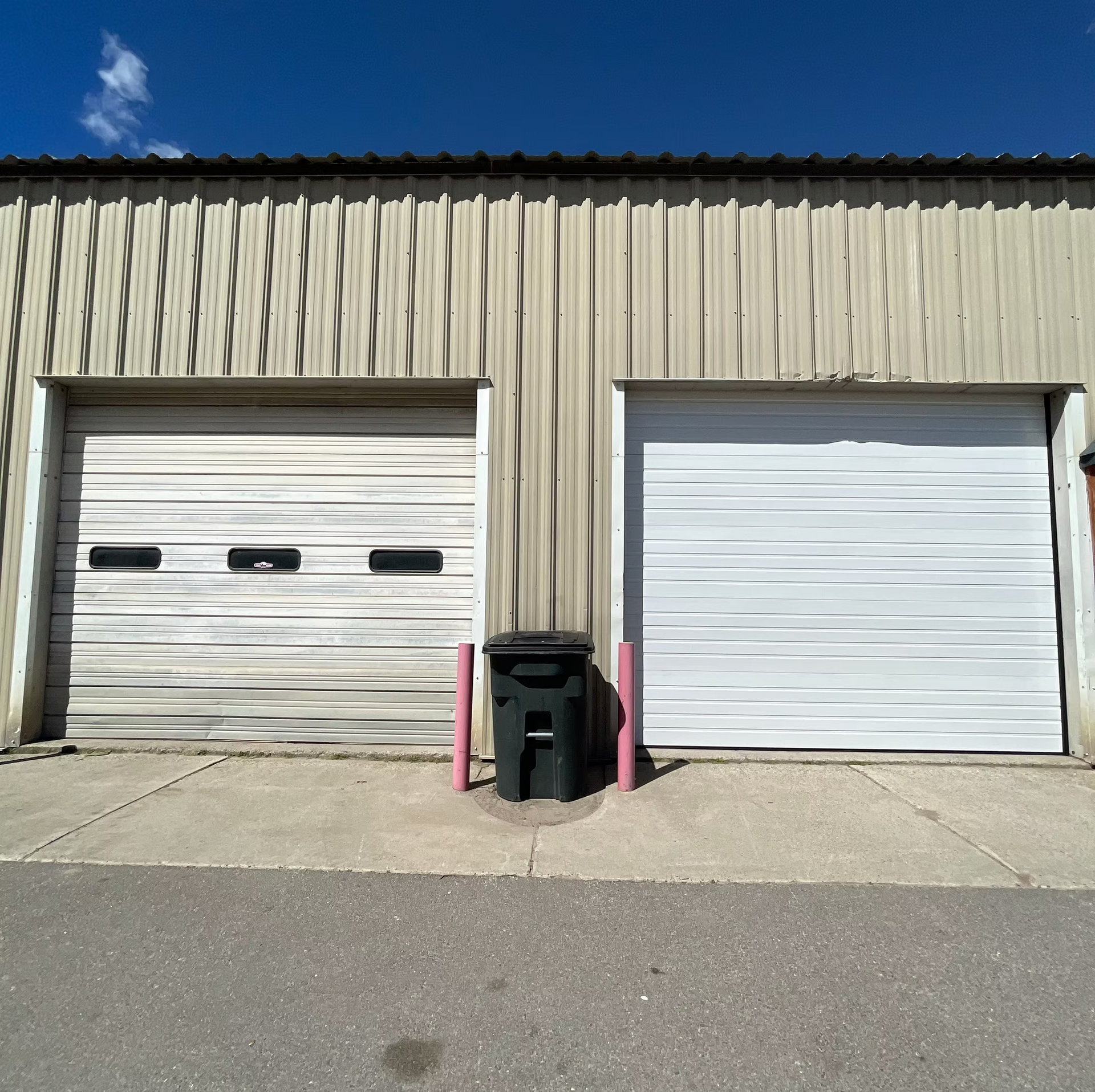 Two white garage doors with a black trash can in front of them