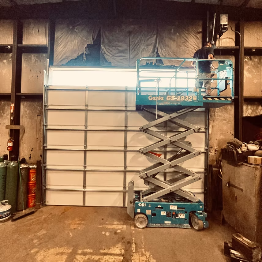 A scissor lift is sitting in front of a garage door.