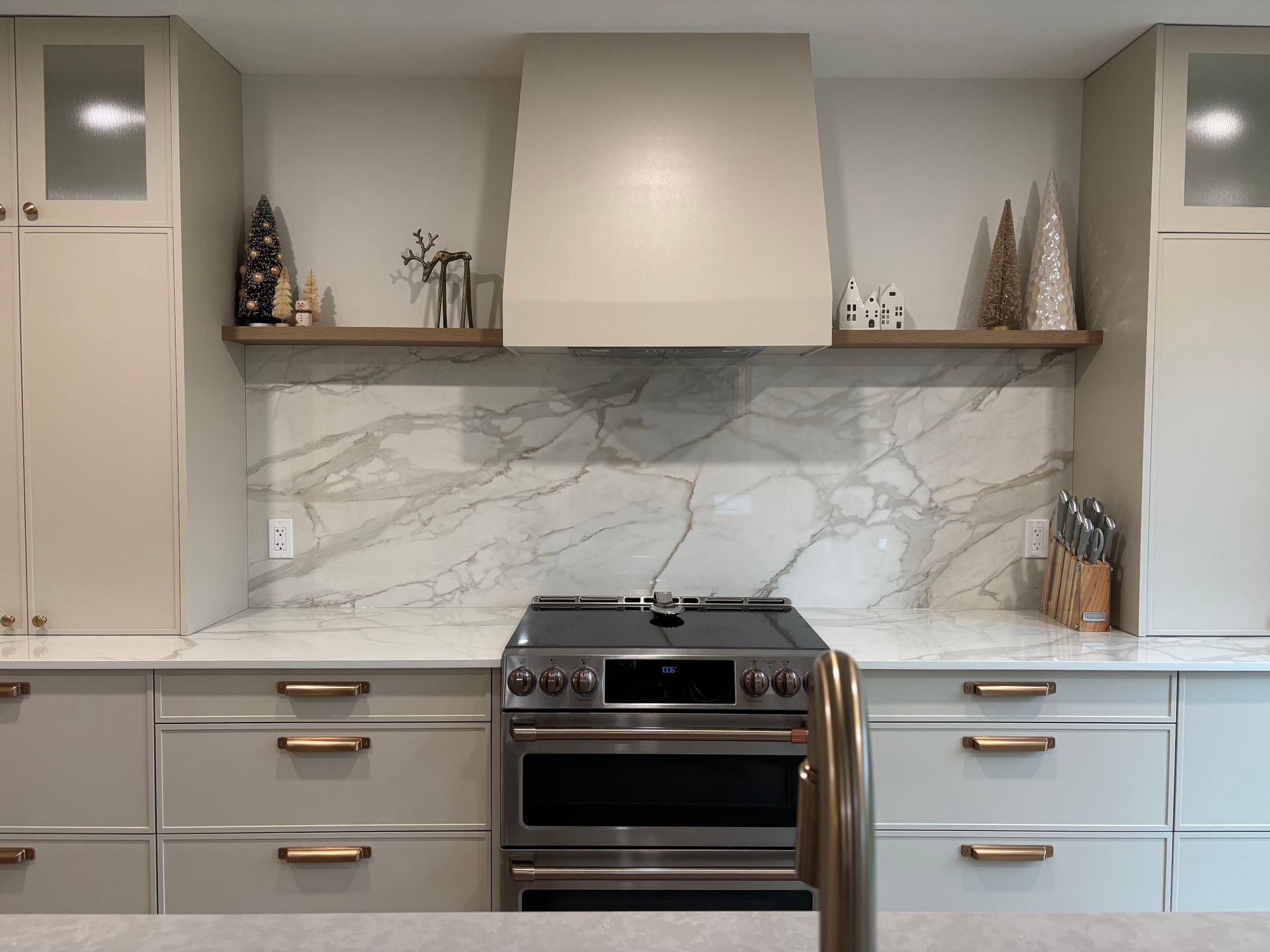 Modern kitchen with marble backsplash, stove, range hood, and light-colored cabinets.