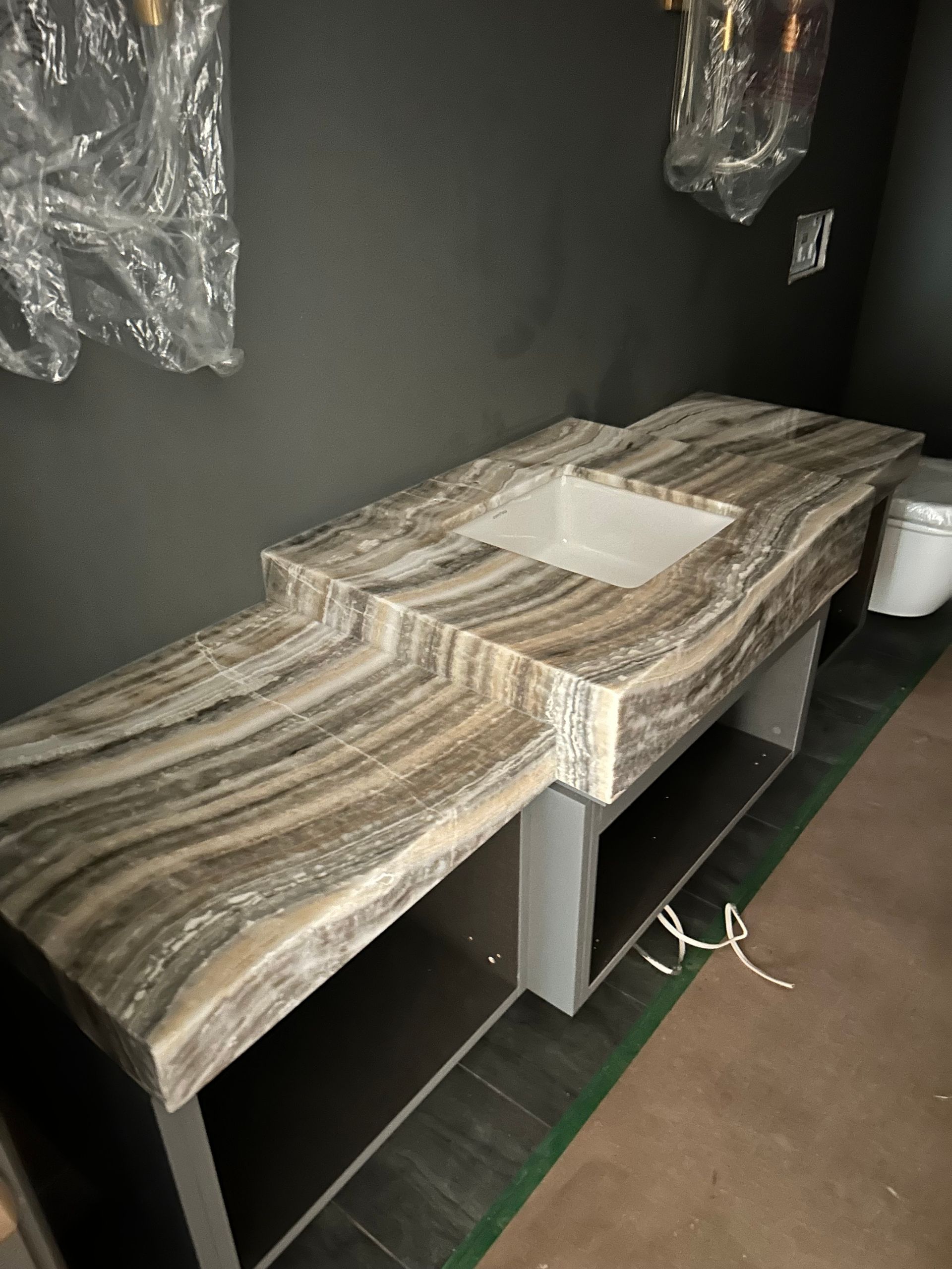 Vanity with light and dark striped countertop, inset sink, and open shelving, against a dark gray wall.