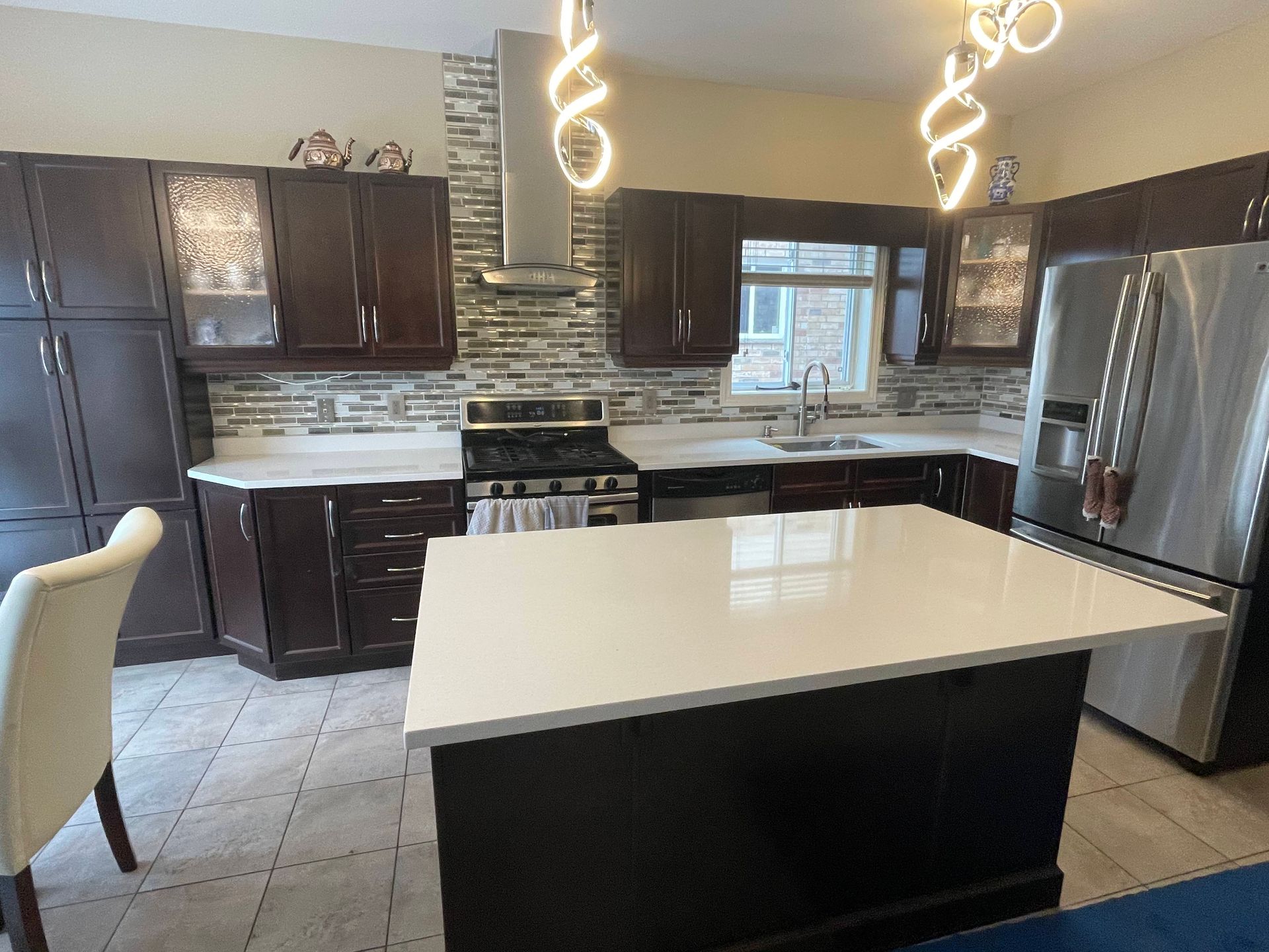 Modern kitchen with dark cabinets, white countertops, stainless steel appliances, and a kitchen island.