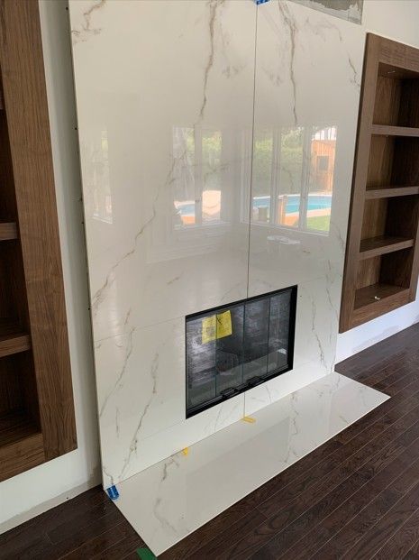 Fireplace with white marble tile, wood built-ins, and dark wood flooring.