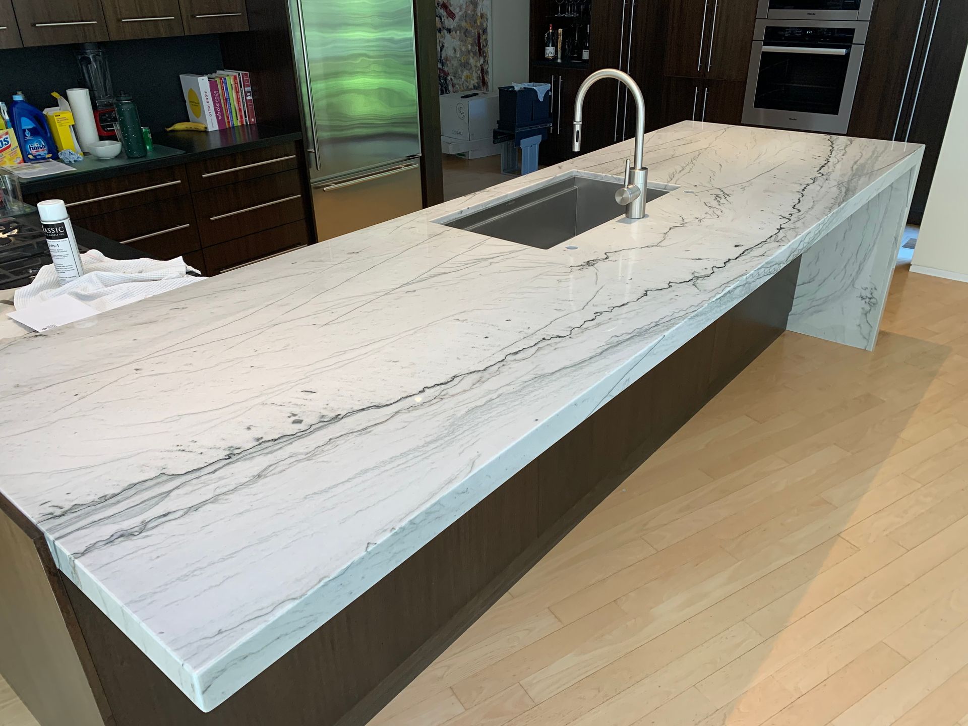 Kitchen island with white countertop, integrated sink, and faucet; wooden cabinetry and floor.