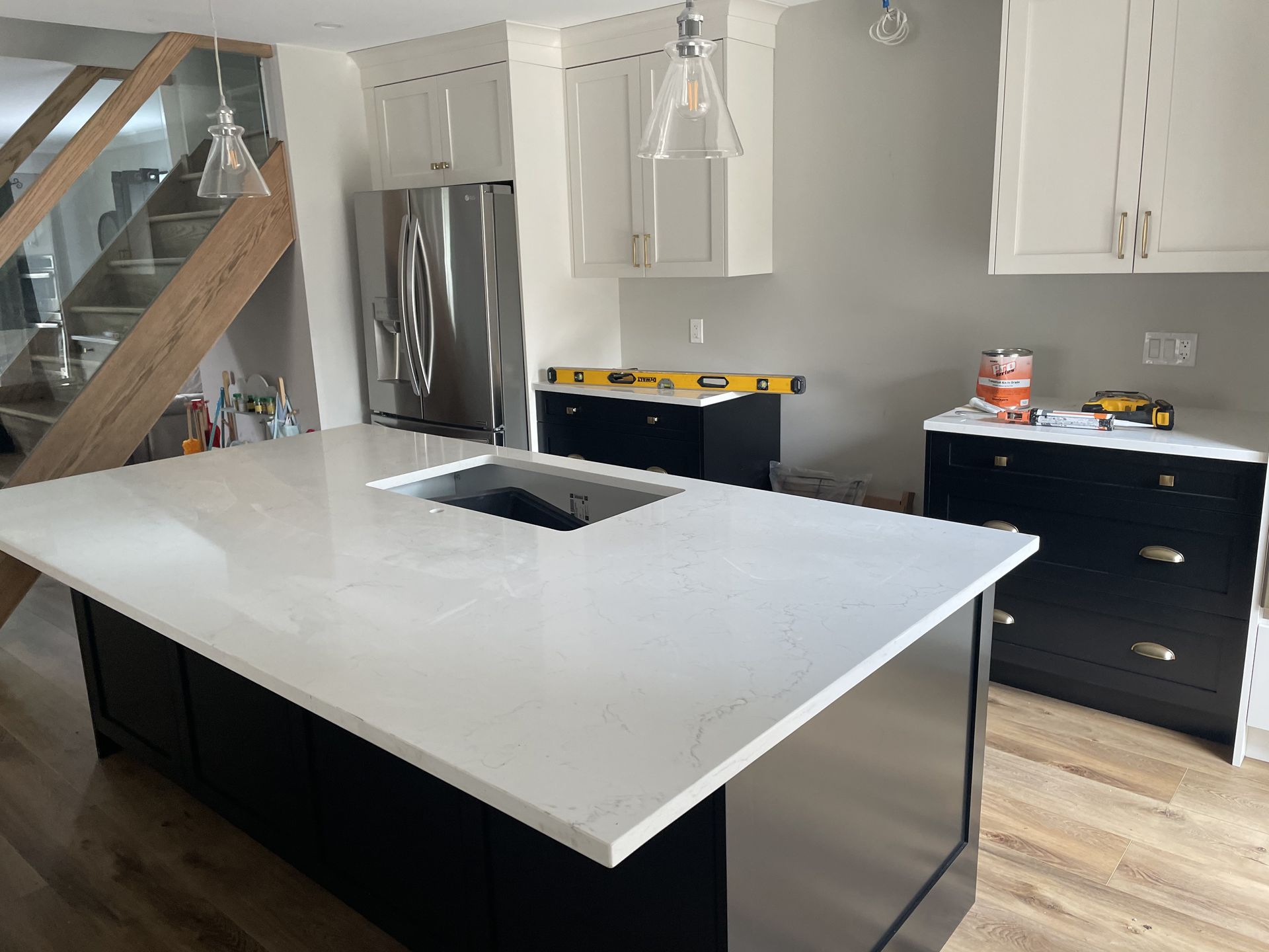 Kitchen with black island, white countertops, black and white cabinets, stainless steel appliances, and a staircase.
