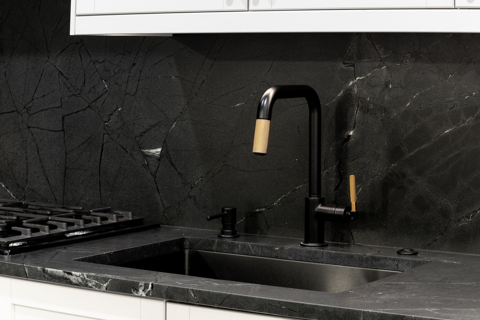 Black faucet and sink in a kitchen with dark stone countertops and backsplash.