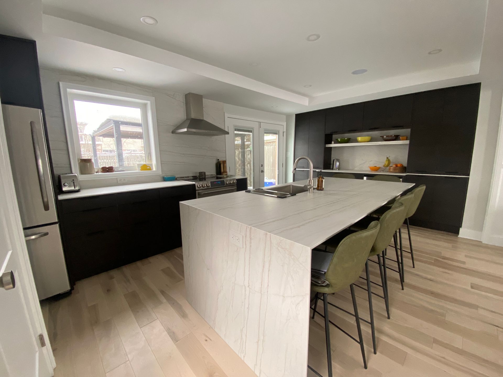 Modern kitchen with white island, dark cabinets, and green bar stools.