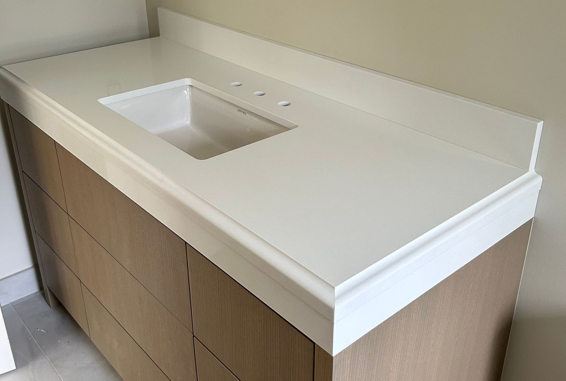 A bathroom vanity with a white counter top and a sink.