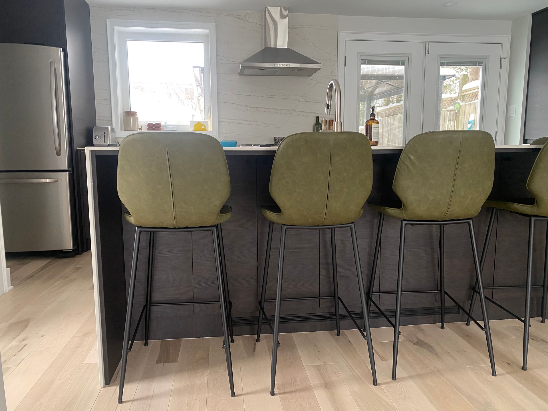 A bar with green bar stools and a stainless steel refrigerator.