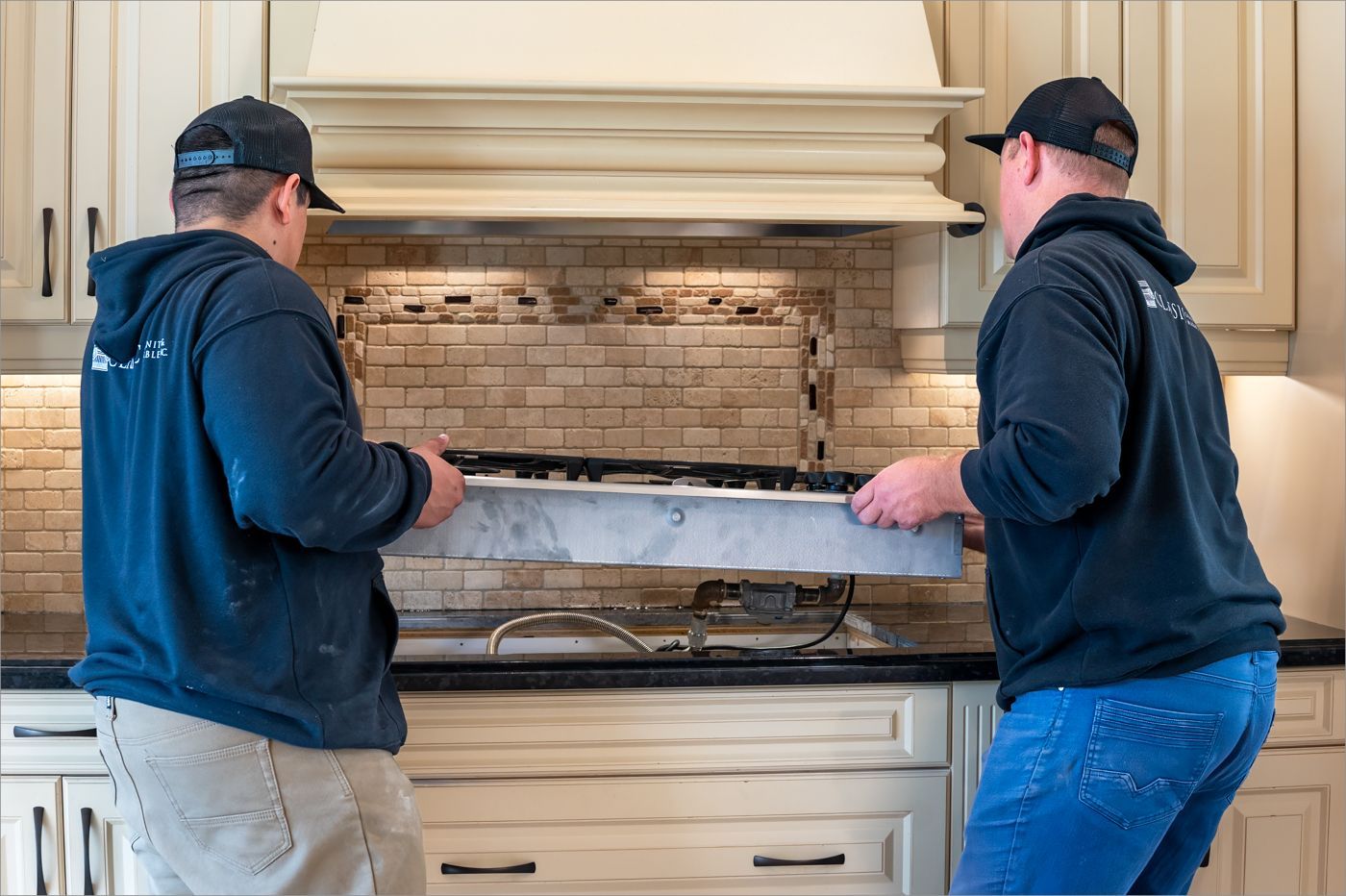 Two men are working on a stove in a kitchen.