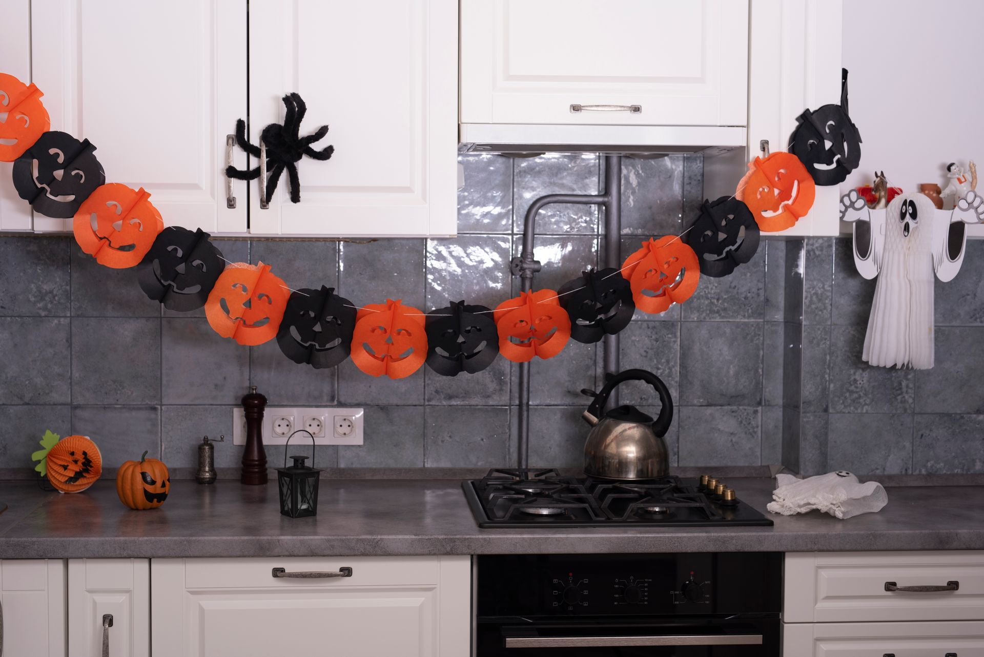 A kitchen decorated for halloween with pumpkins and ghosts hanging from the ceiling.