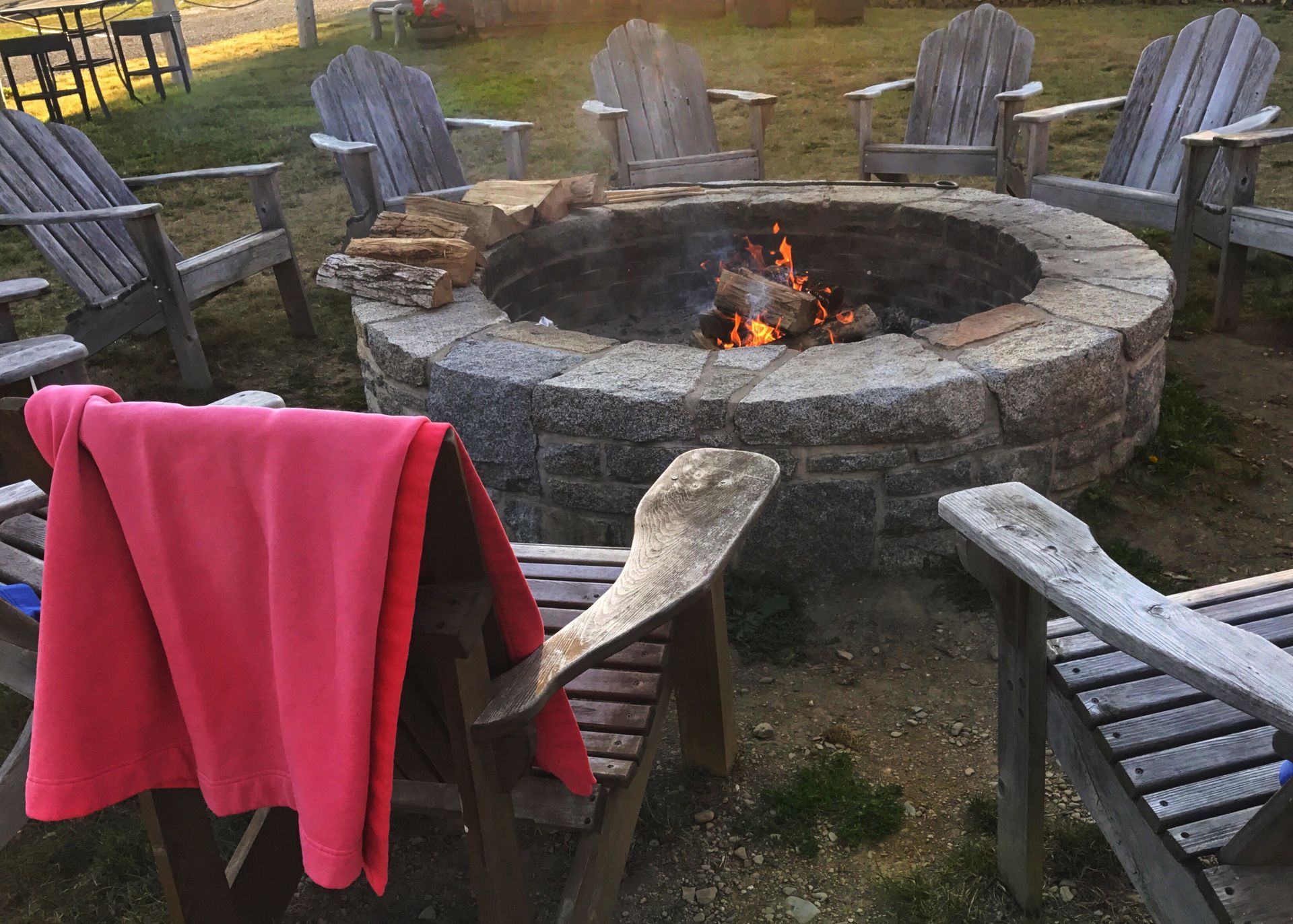 A fire pit surrounded by wooden chairs and a pink blanket.