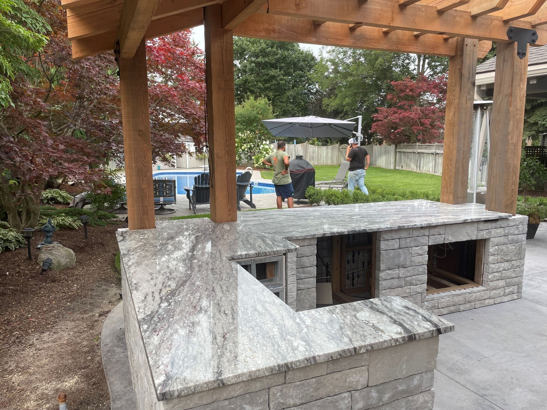 A group of people are standing under a pergola in a backyard.