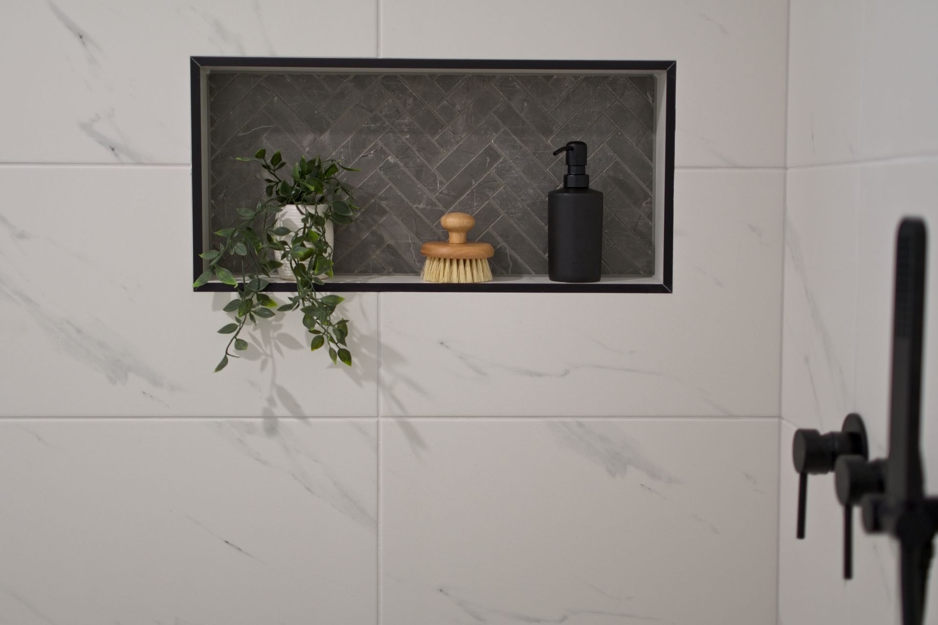 There is a shelf in the shower with a plant and a bottle of soap.