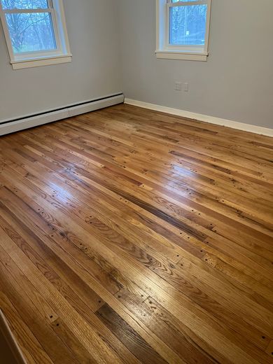 A bedroom with hardwood floors and two windows.