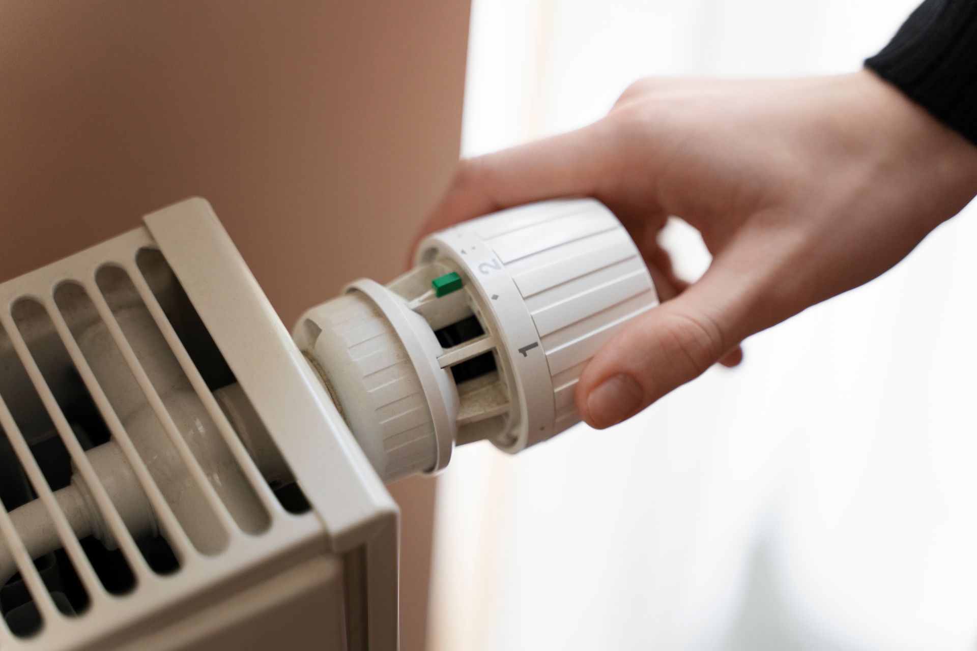 Hand adjusting the temperature dial on a white radiator.