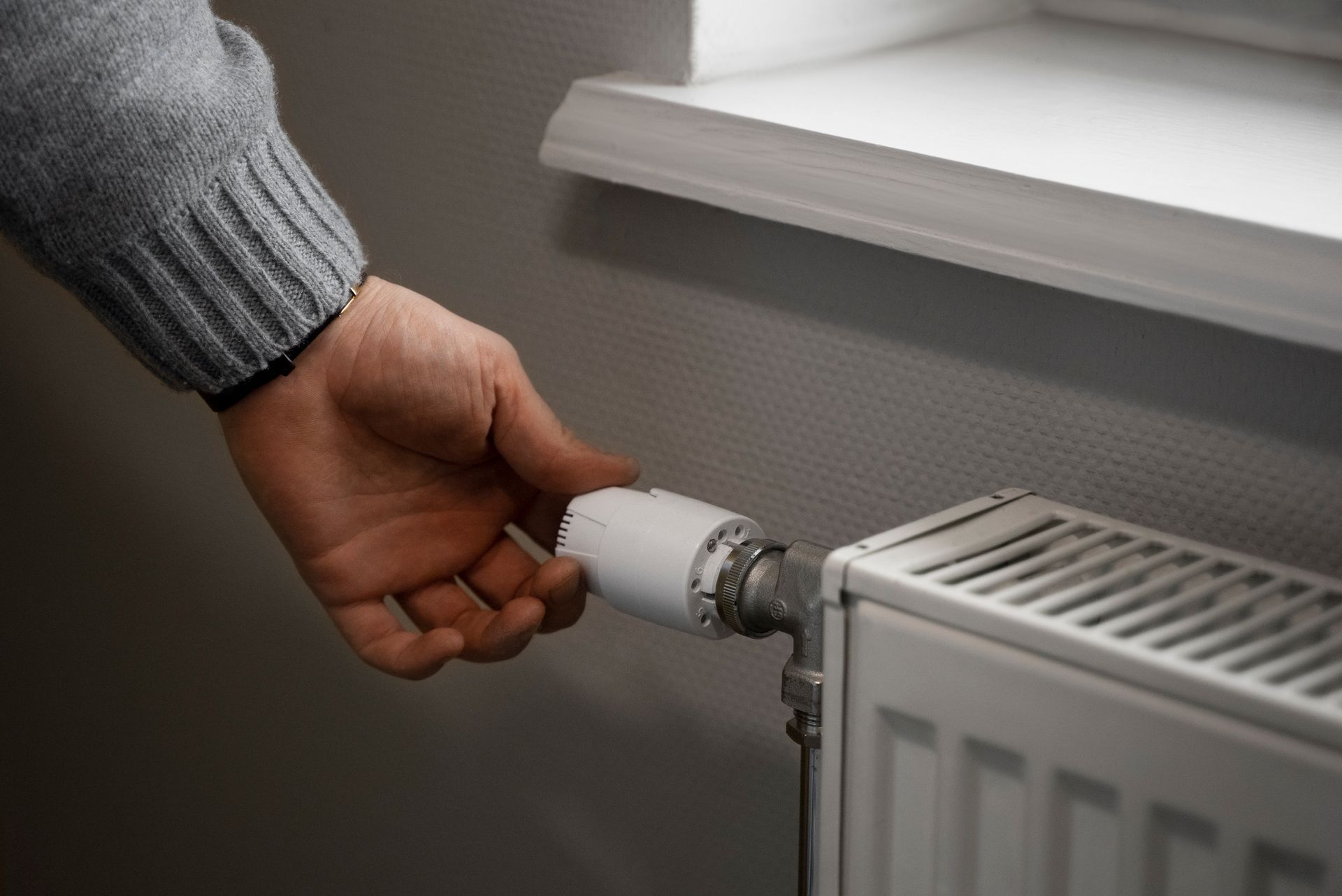 A person is adjusting the thermostat on a radiator.
