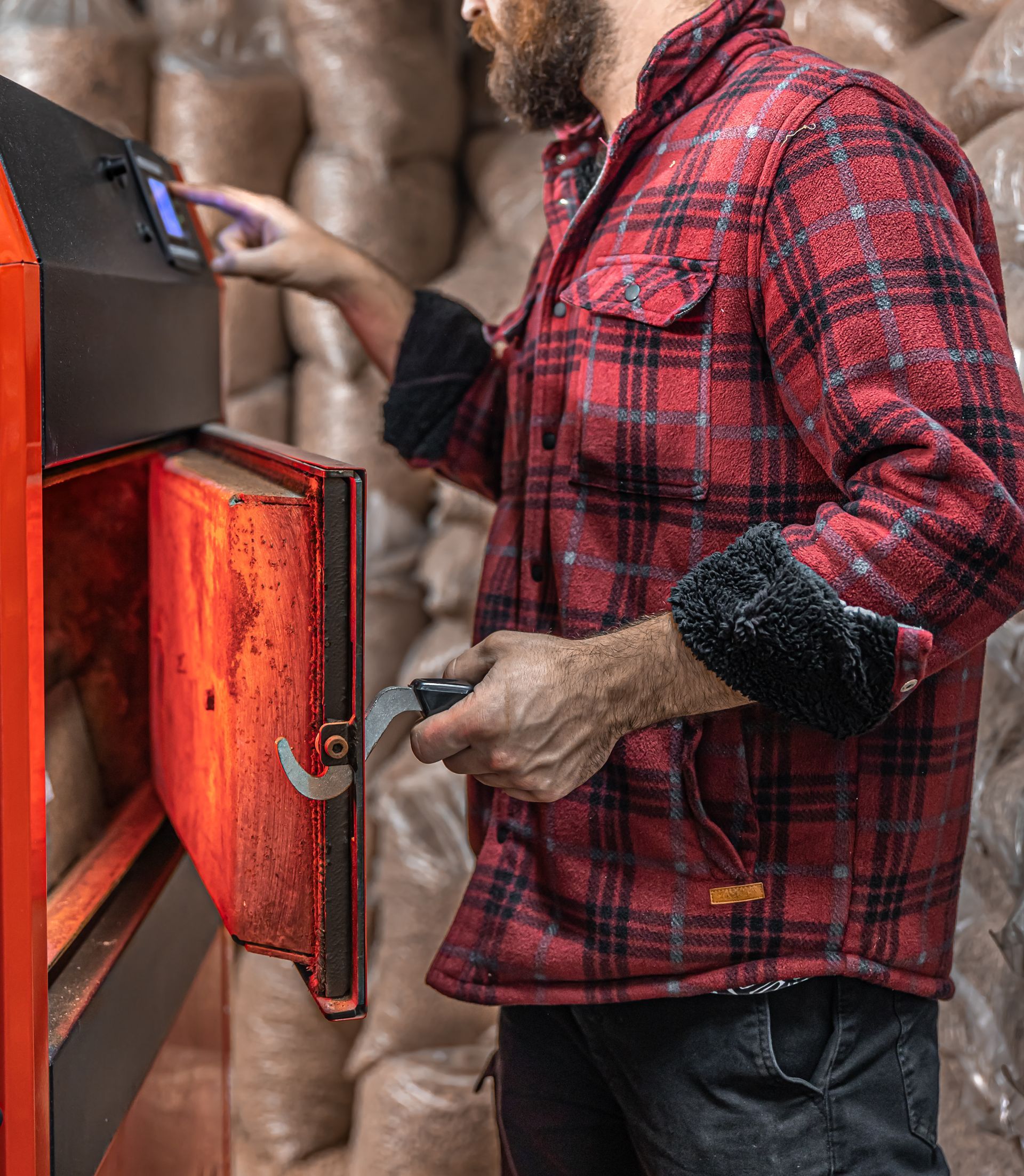 Man in plaid jacket operates wood pellet stove, opening the door and pressing controls.
