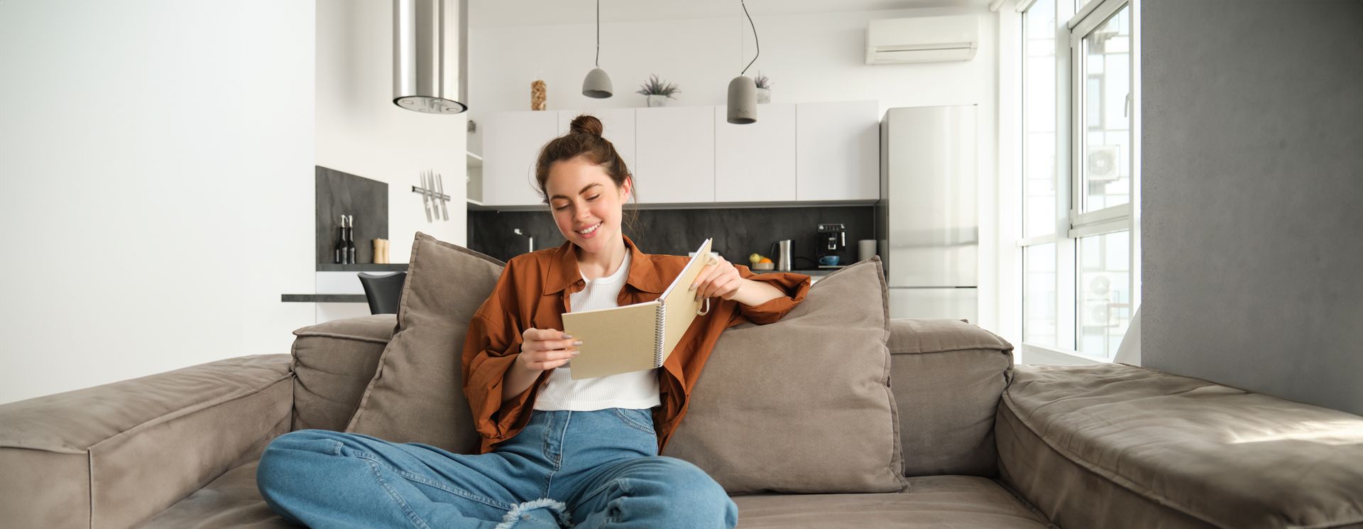 Person reading a paper on a gray sofa in a bright modern living room