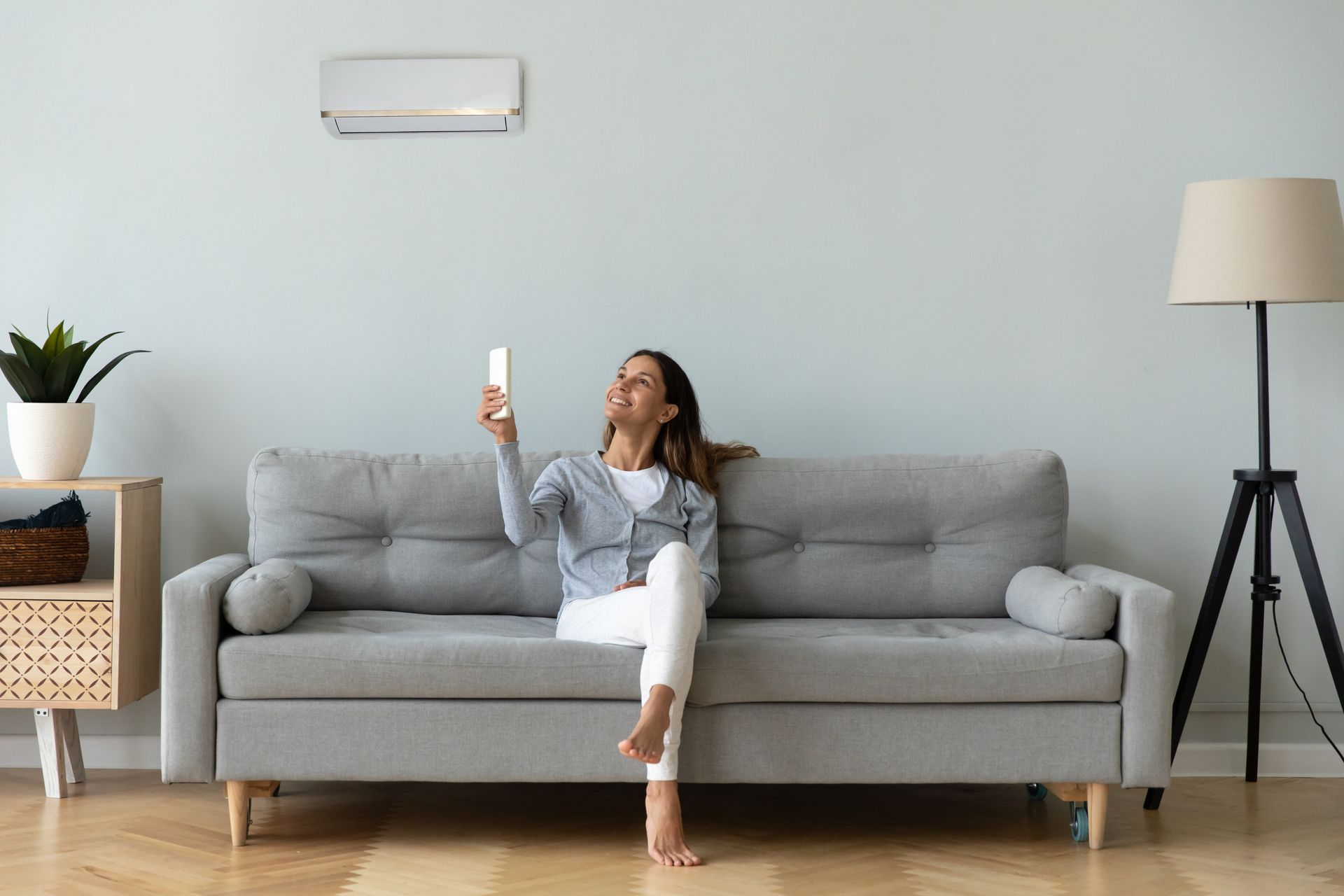 Woman sitting on a gray sofa, holding up a phone in a bright living room