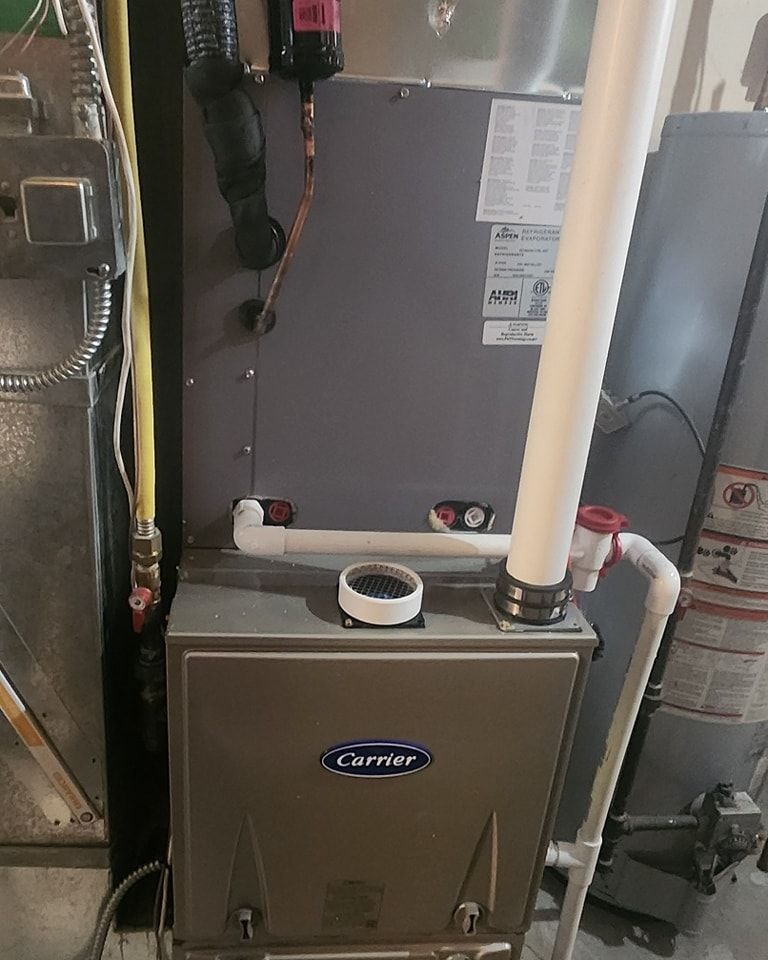 A Carrier furnace in a utility room with white PVC pipes and a hot water heater visible.