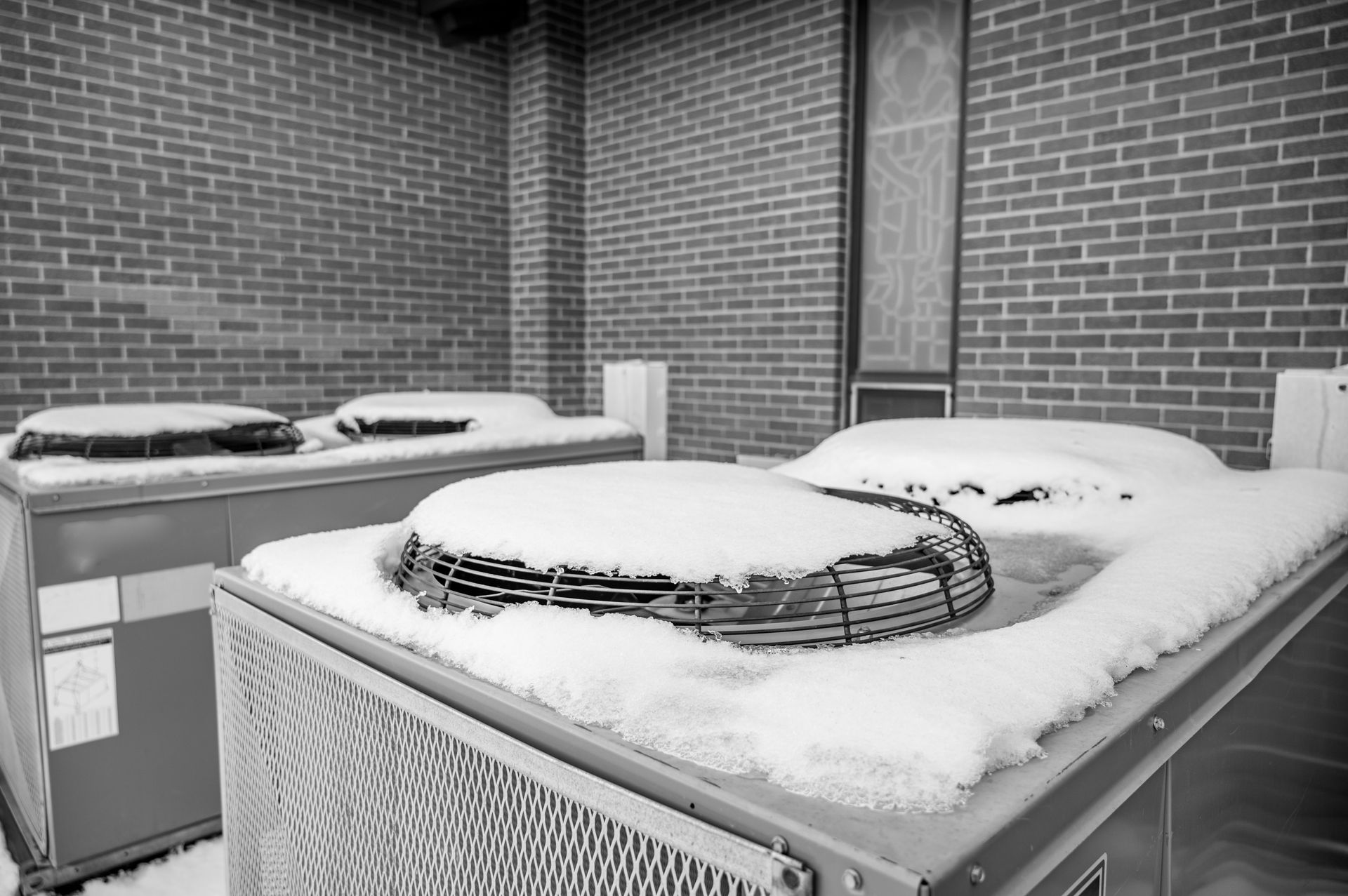 Snow-covered rooftop air conditioning units against a brick wall.