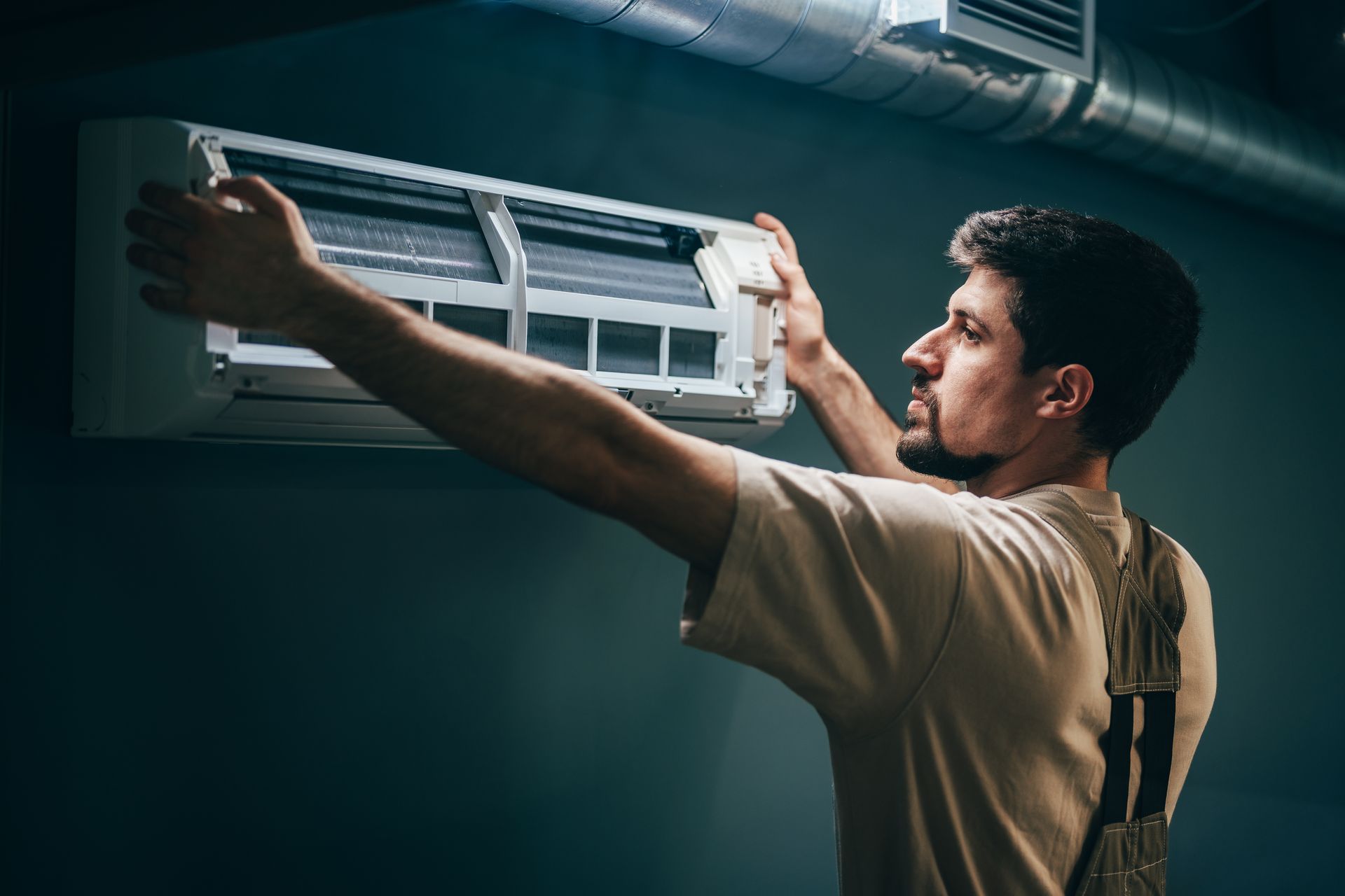 Technician cleaning a wall-mounted air conditioner with a cloth in a dim room