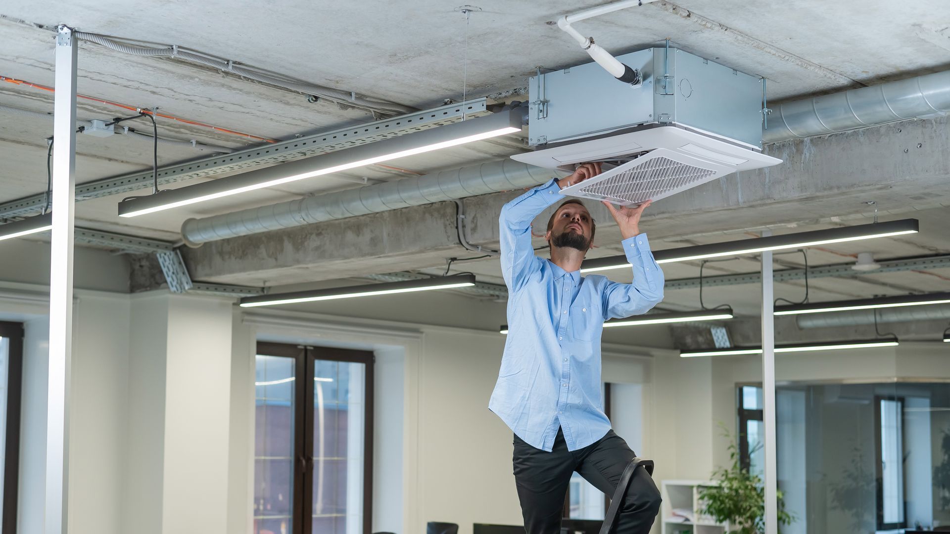 A man is fixing a ceiling fan in an office.