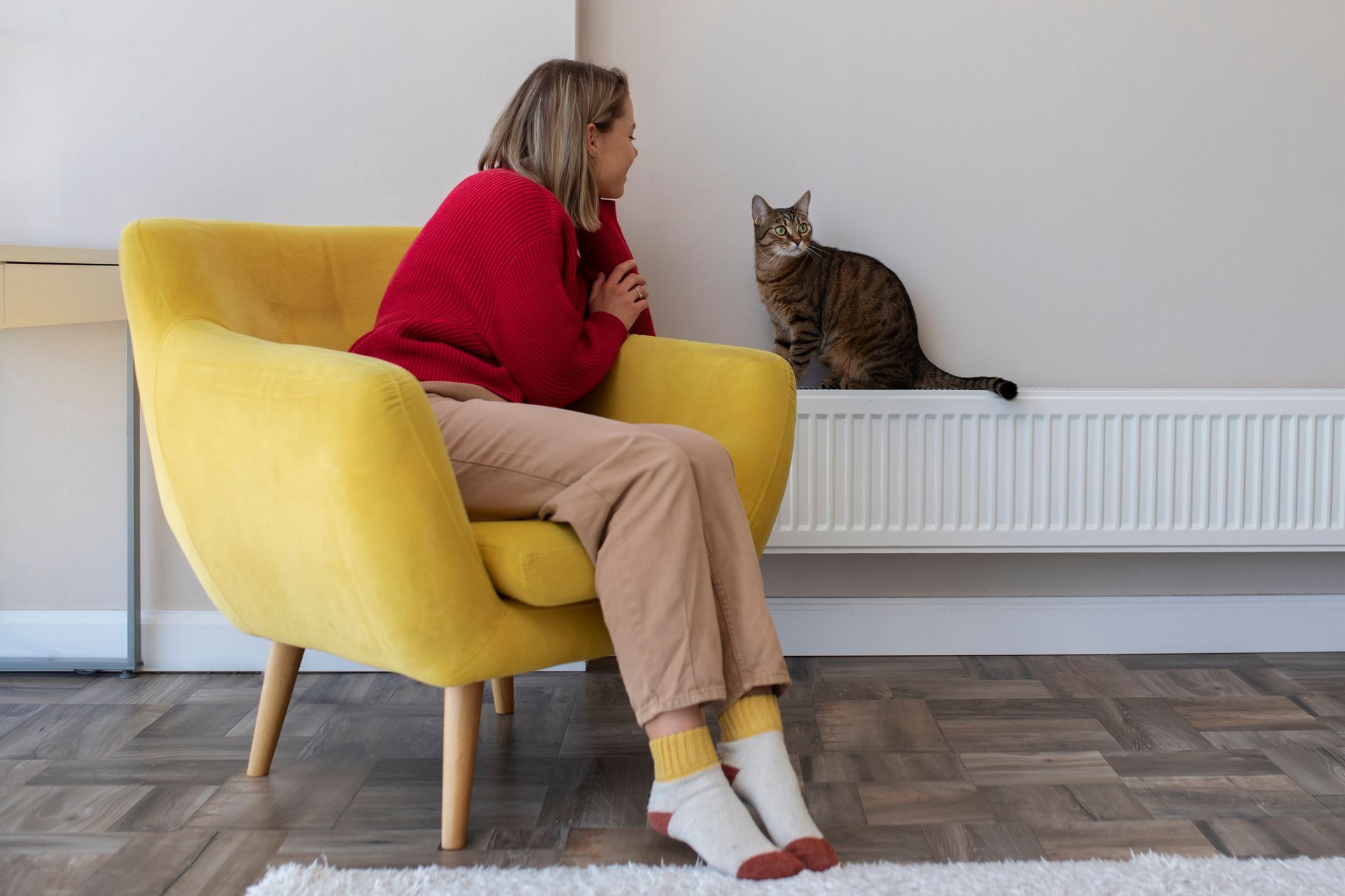 A woman is sitting in a yellow chair next to a cat.