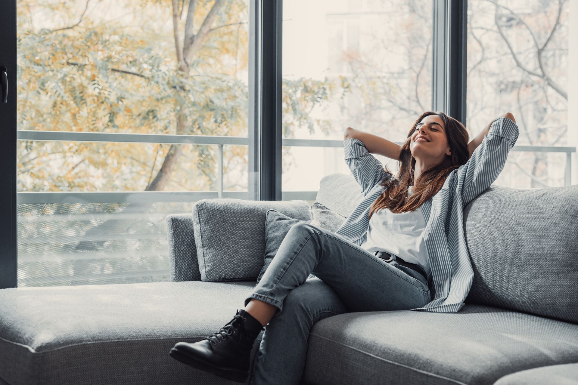 A woman is sitting on a couch in front of a window.