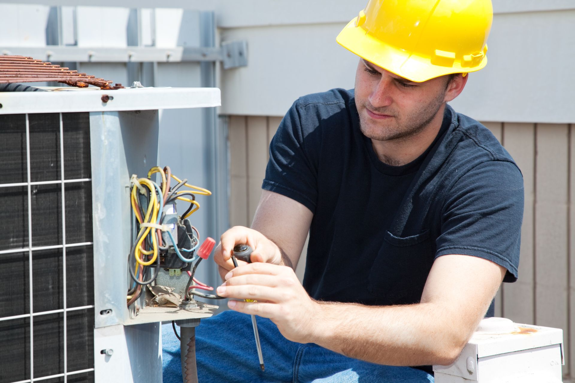 A man wearing a hard hat is working on an air conditioner.