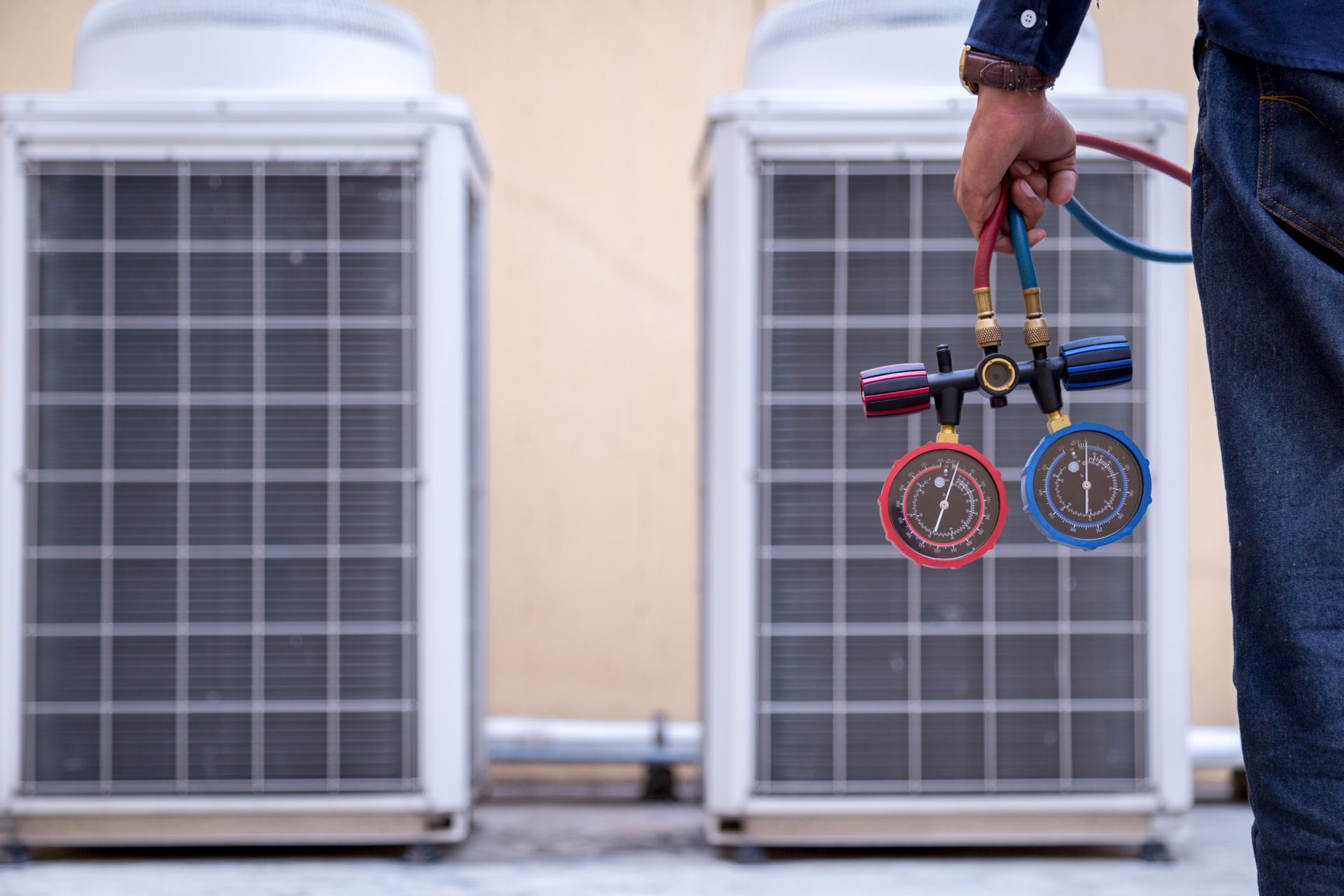 A man is holding two gauges in front of two air conditioners.
