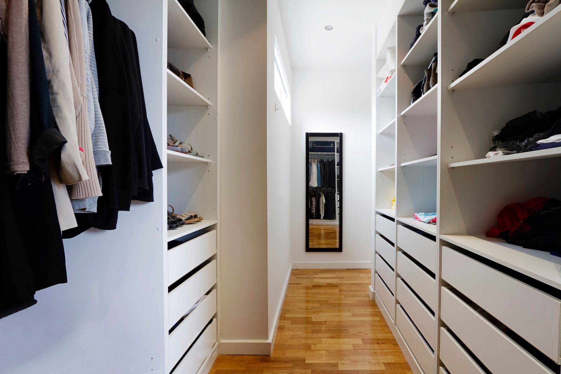 A walk in closet with lots of shelves and drawers and a mirror.