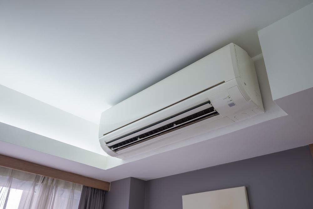 Wall-mounted split air conditioning unit installed near the ceiling in a modern room with white wall